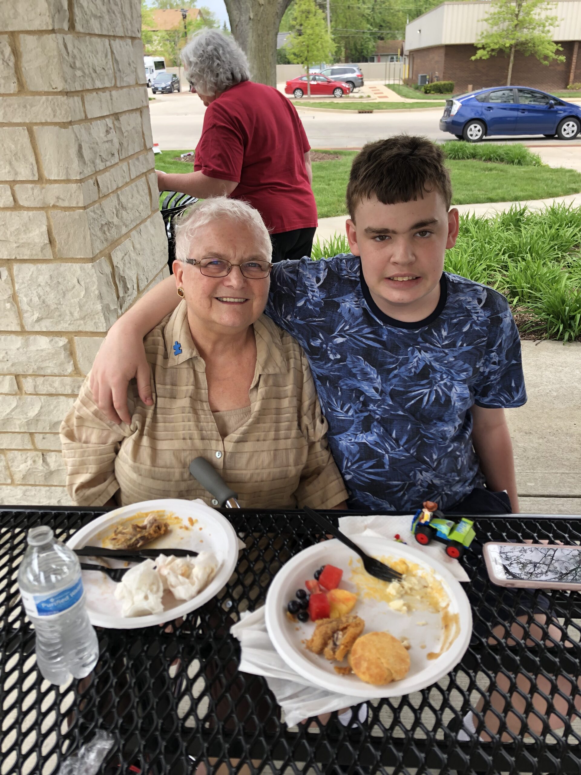 Two people pose happily together for the photo while sitting at a picnic table. There are plates with a little bit of food left in front of both of them.